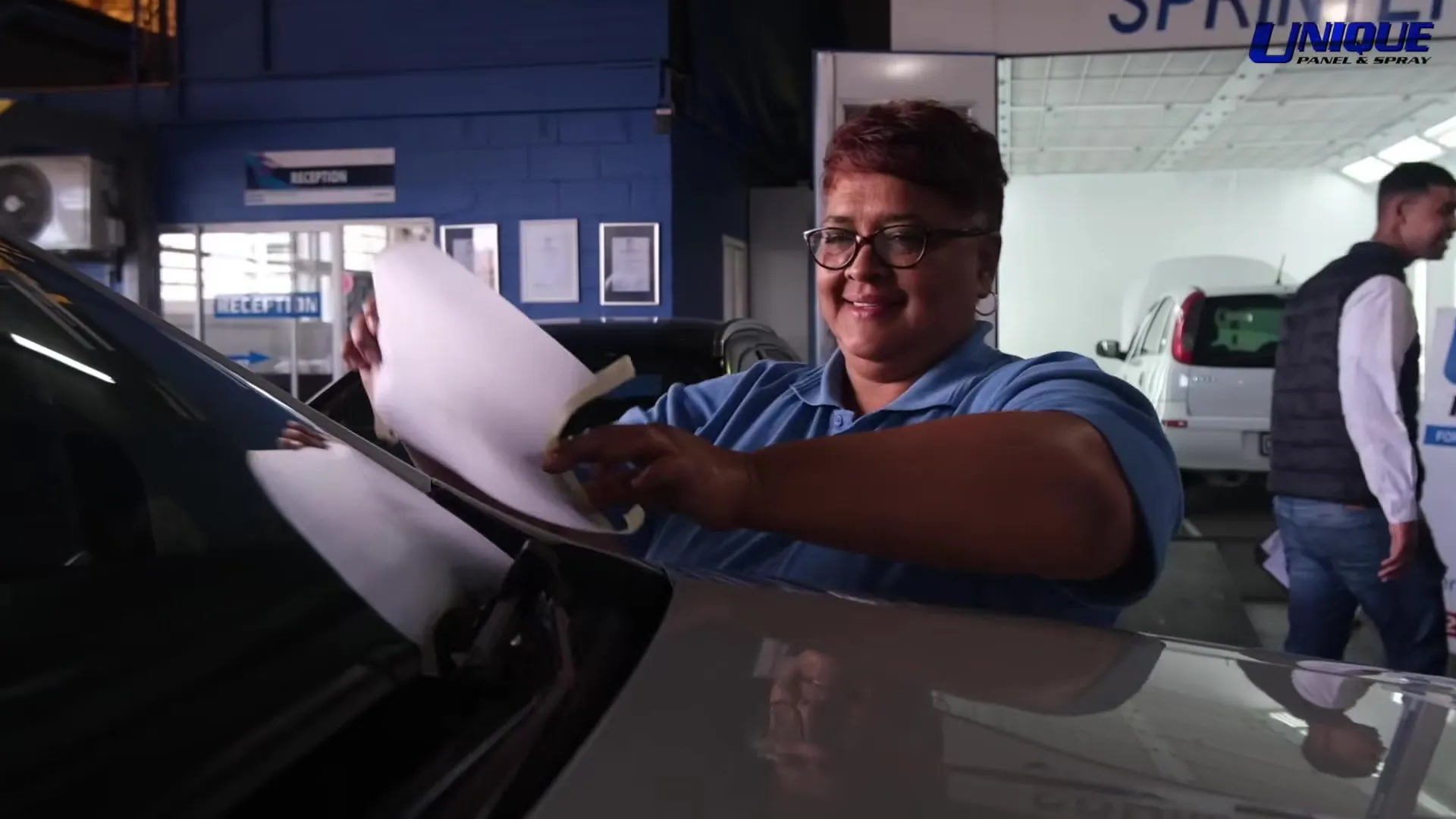 Unique Panel & Spray staff member with paperwork beside a car booked in for repair